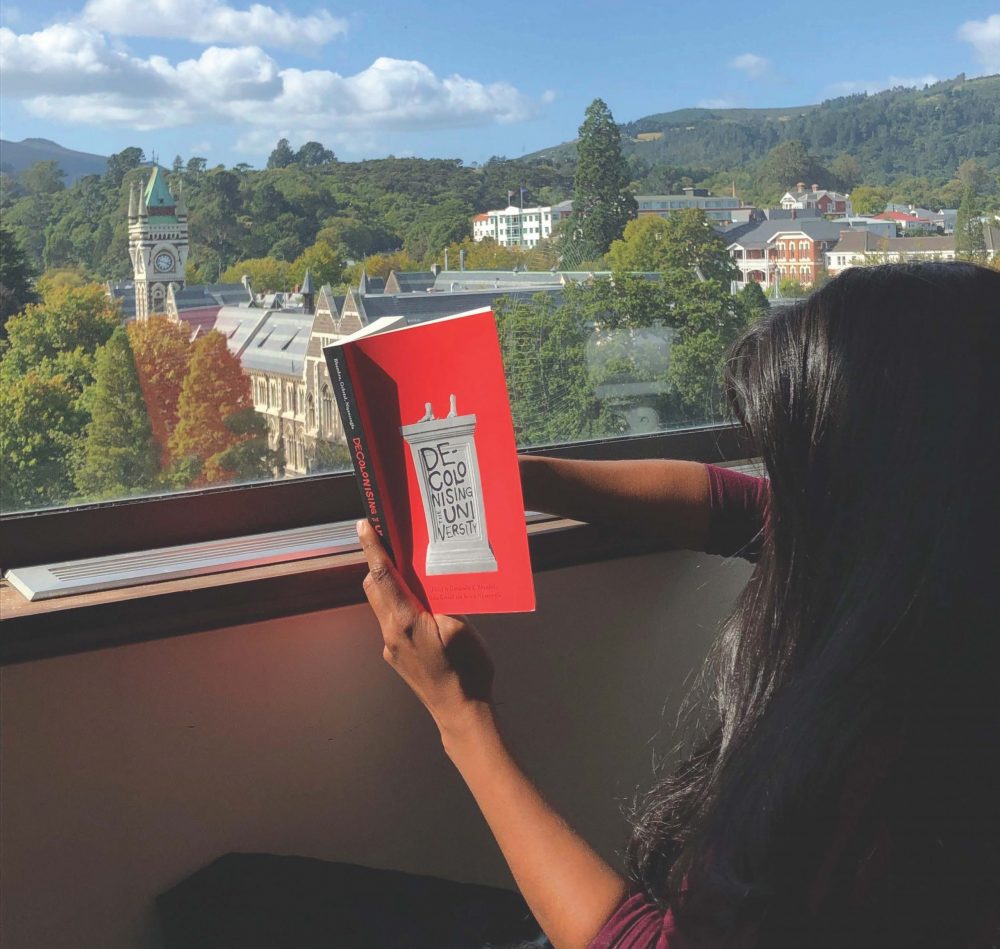 women reading a book titled 'Decolonising University' at a window.