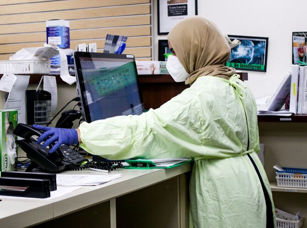 A masked person in medical scrubs answers the phone