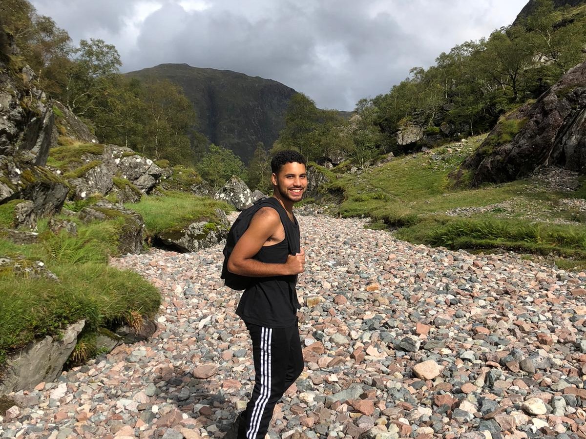 A man with a rucksack stands on a rocky path surrounded by hills
