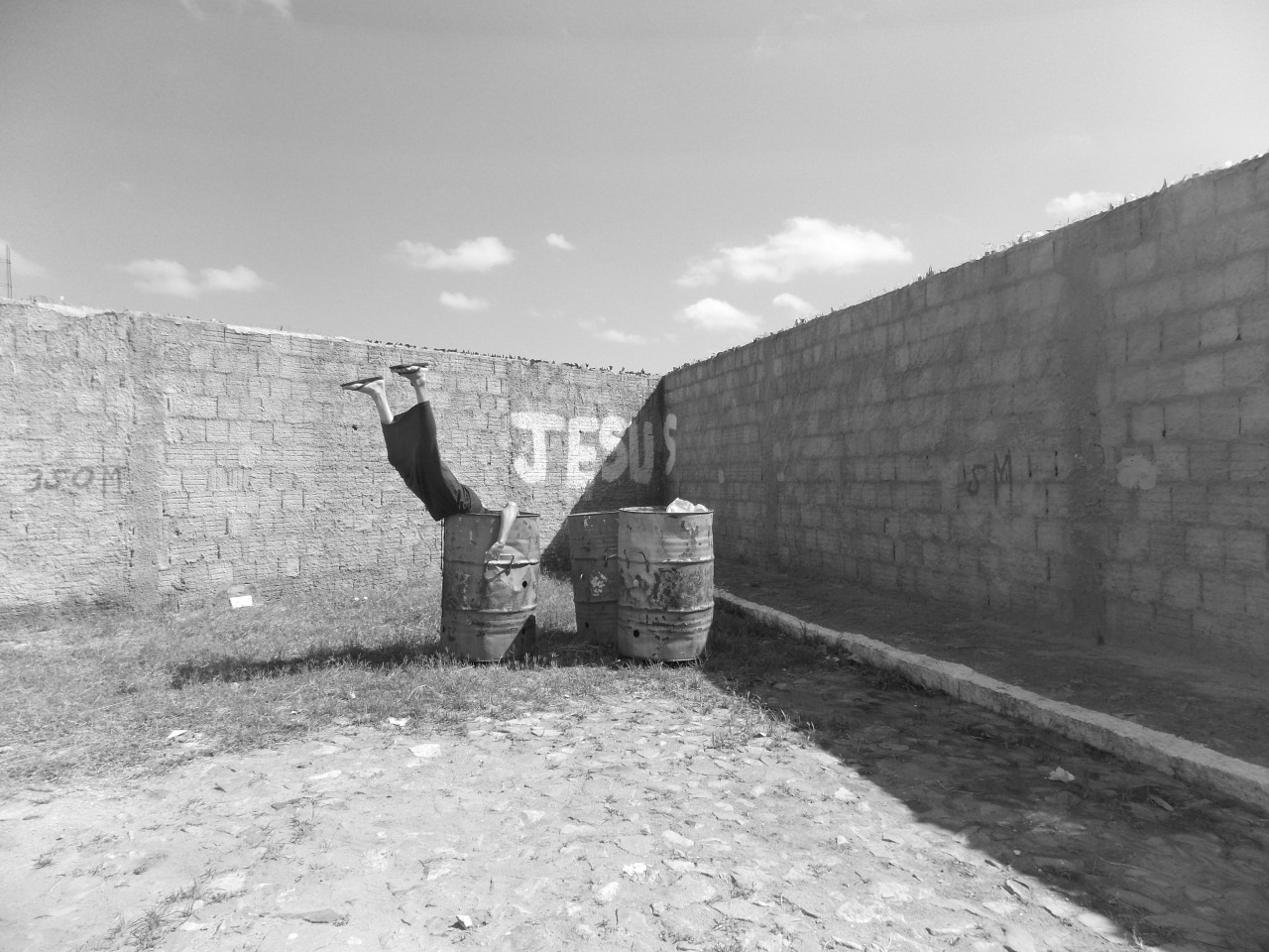Legs stick out of a bin in front of graffiti that reads 'Jesus'