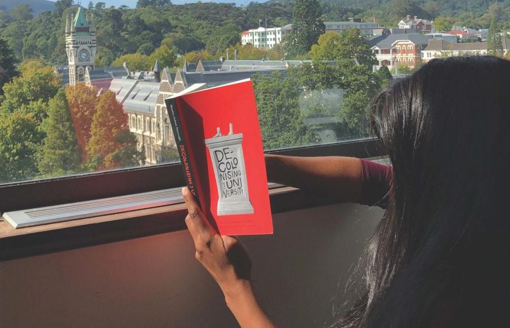 women reading a book titled 'Decolonising University' at a window.