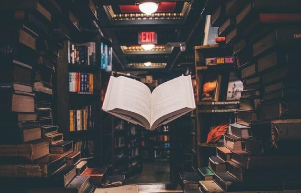 A floating open book, surrounded by stacks of other books
