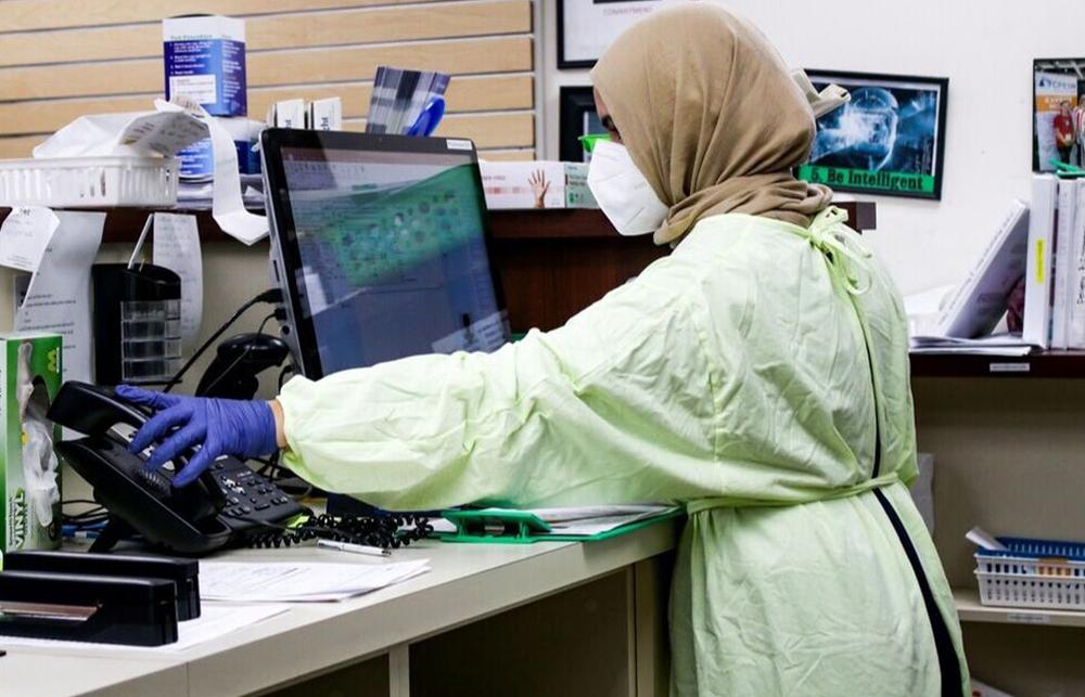 A masked person in medical scrubs answers the phone