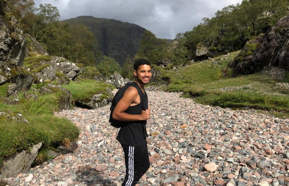 A man with a rucksack stands on a rocky path surrounded by hills