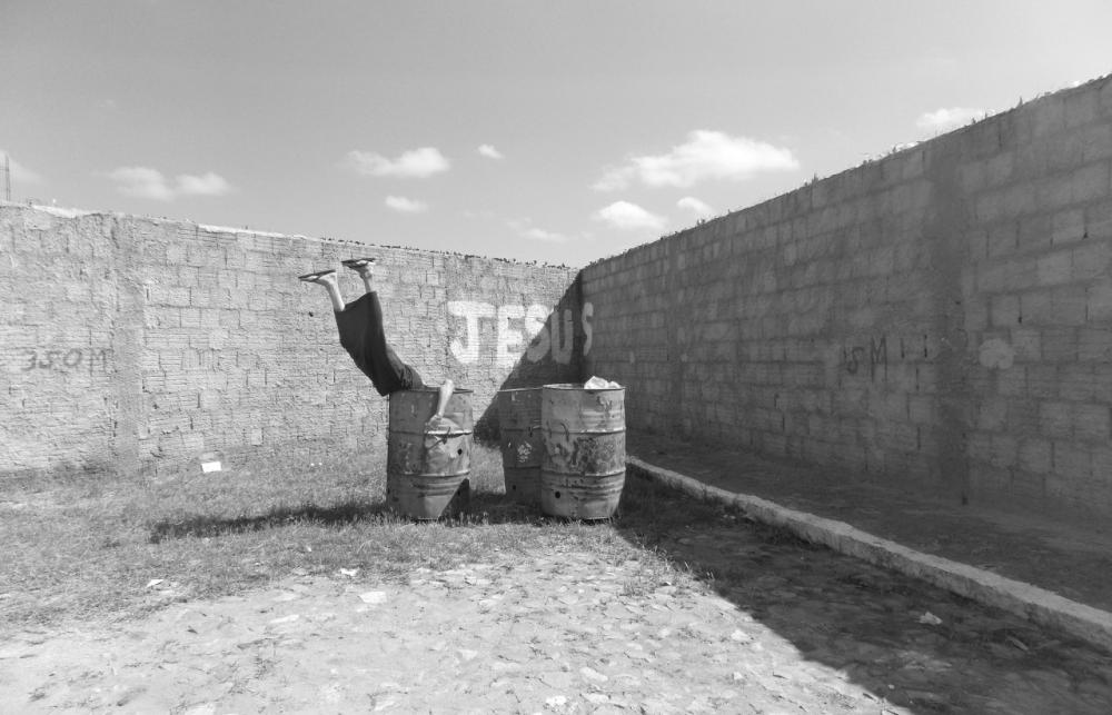 Legs stick out of a bin in front of graffiti that reads 'Jesus'